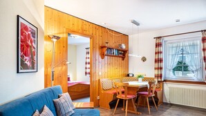 Um quarto aconchegante com um sofá azul, paredes de madeira, uma área de jantar com cadeiras, uma mesa e uma janela com cortinas.
