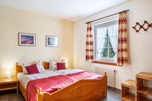 A bedroom with a wooden bed, a window with patterned curtains, a radiator, and two framed pictures on the wall. - Apartment 'Aretz' with Mountain View, Private Terrace and Wi-Fi (Feldberg (Schwarzwald))