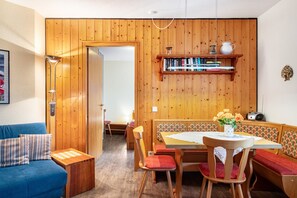 A room with a wooden wall, a dining table with chairs, a bench, a bookshelf, and a small table with a vase. - Apartment 'Aretz' with Mountain View, Private Terrace and Wi-Fi (Feldberg (Schwarzwald))