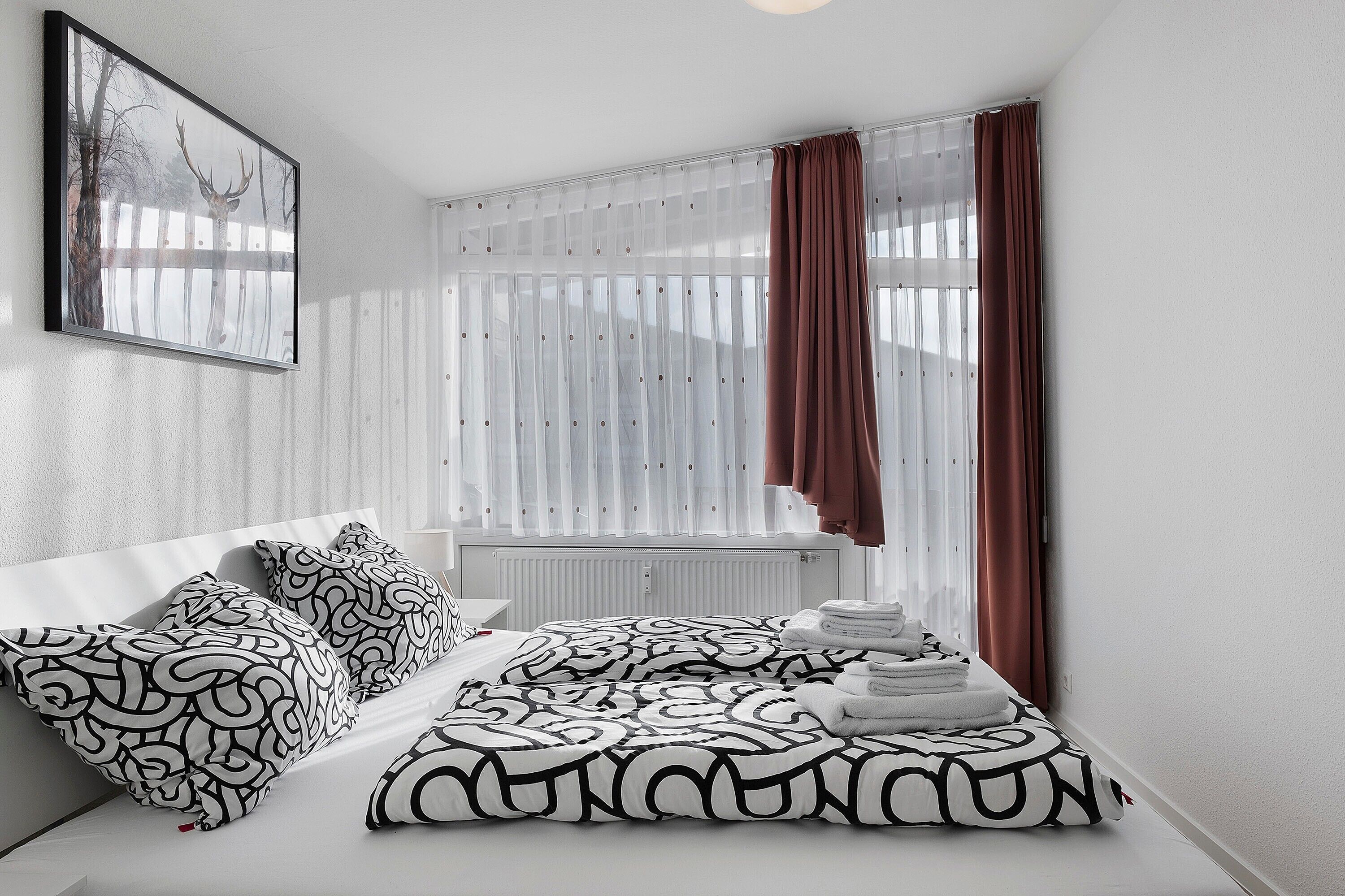 A modern bedroom with a bed, pillows, a radiator, and a window with curtains.