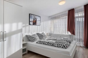 Ein modernes Schlafzimmer mit Bett, Nachttischen, einem Kleiderschrank, einer Heizung und einem Fenster mit Vorhängen.