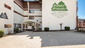 Een gebouw met een bordje waarop 'Kurhotel Schluchsee' staat, wat aangeeft dat het een hotel is met voorzieningen zoals een sauna, doktersruimte en restaurant.