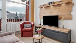 Een moderne woonkamer met een televisie, houten wandpaneel, een rode fauteuil en uitzicht op een besneeerd landschap.