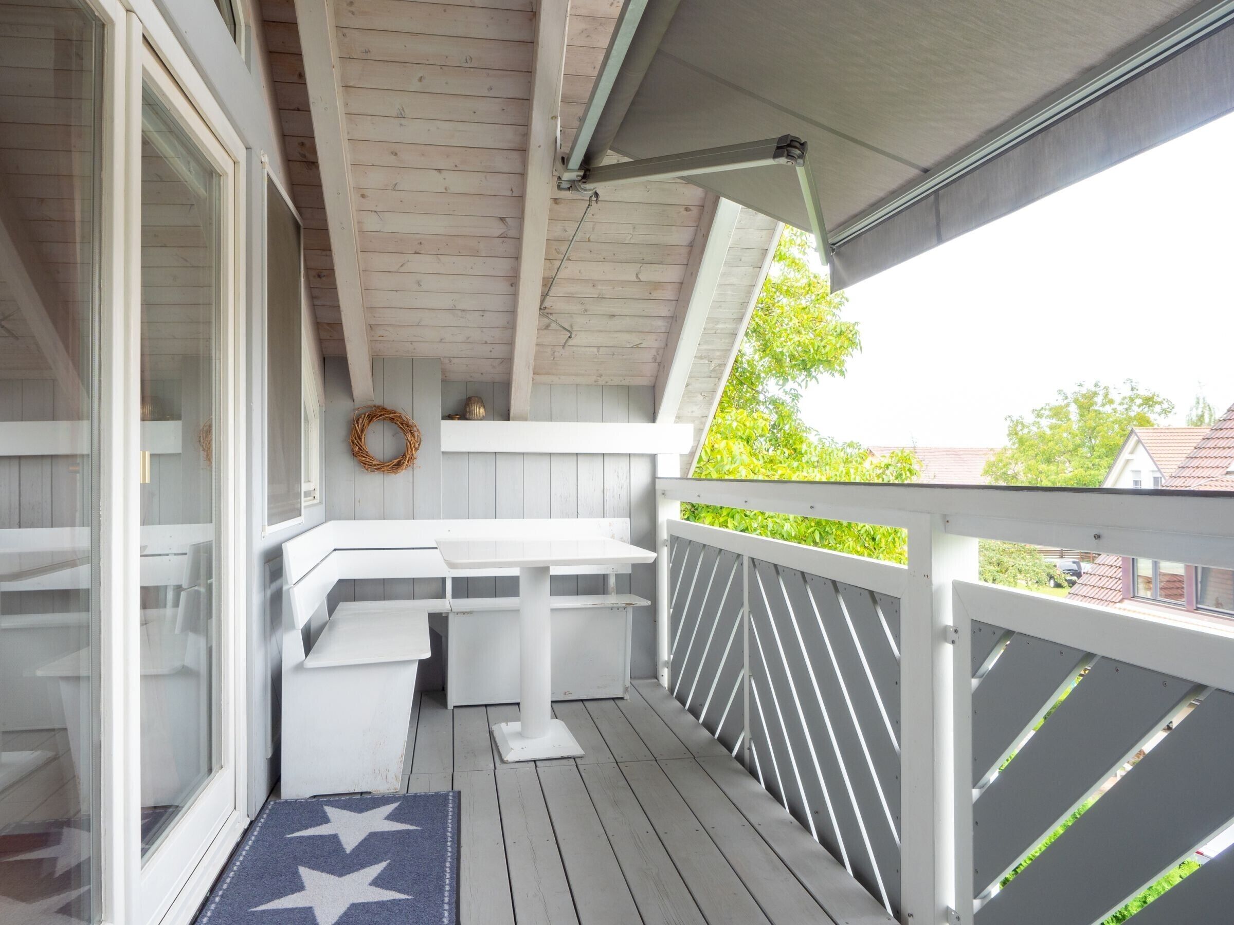A covered porch with a white bench, a small table, and a decorative wreath on the wall.