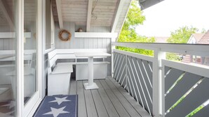 A covered porch with a white bench, a small table, and a decorative wreath on the wall. - Apartment 'Denn' with Shared Garden, Balcony and Wi-Fi (Langenargen)