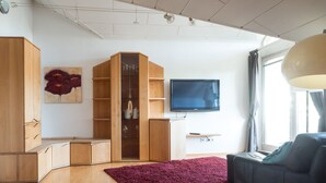 A modern living room with wooden furniture, a flat-screen TV, and a large window. - Apartment 'Denn' with Shared Garden, Balcony and Wi-Fi (Langenargen)