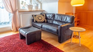 A modern living room with a leather sofa, a red rug, a small round table, and a yellow lamp. - Apartment 'Denn' with Shared Garden, Balcony and Wi-Fi (Langenargen)