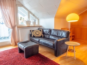 Uma sala de estar moderna com um sofá de couro, um tapete vermelho, uma mesa redonda pequena e um abajur amarelo.