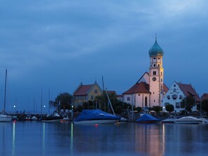 En havnefront med en markant kirke, der har et tårn og en spir, omgivet af rolige vand og både.