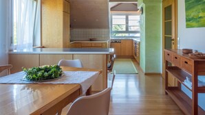 A modern kitchen with wooden cabinets, a dining area with a table and chairs, and a view of the adjacent living space. - Apartment 'Denn' with Shared Garden, Balcony and Wi-Fi (Langenargen)