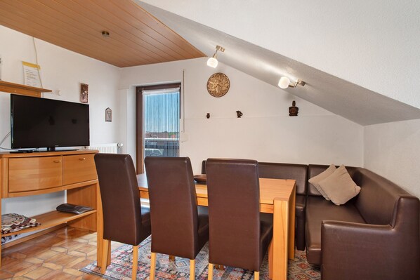 A dining area with a wooden table, chairs, and a television on a stand.