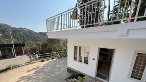 A two-story building with a balcony, potted plants, and a view of a mountainous landscape. - Aloha Homestay Munnar (Anachal)