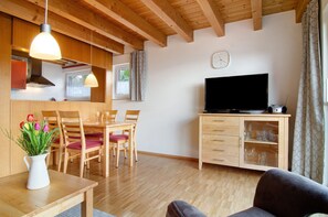 Ein Wohnzimmer mit Essbereich, Holzbalkendecke, Flachbildfernseher und einer Vitrine mit Gläsern.