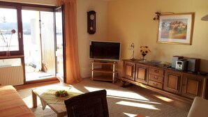 Ein Wohnzimmer mit Fernseher, einer Uhr, einem Gemälde und einem Essbereich mit Tisch und Stühlen.