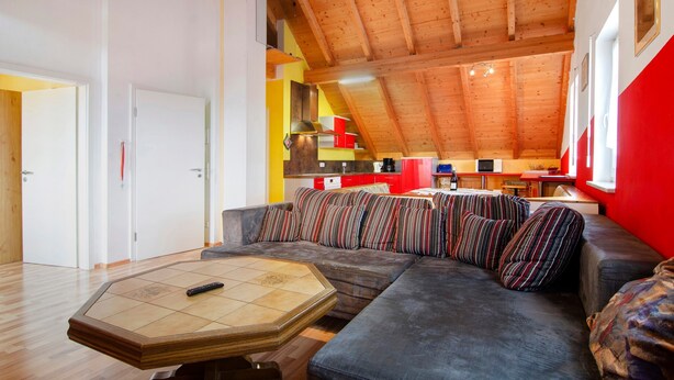 A modern interior with a wooden ceiling, a sofa with striped cushions, and a kitchen area in the background. - Saupp Apartment with Garden and Wi-Fi (Immenstaad am Bodensee)