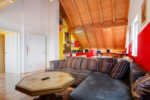 Un interior moderno con techo de madera, un sofá con cojines a rayas y una cocina al fondo.