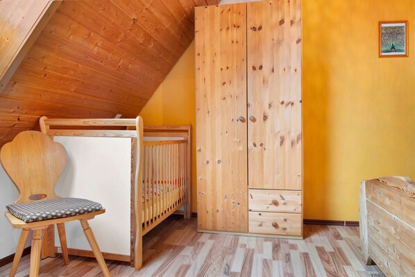 Una habitación con techo inclinado, una cuna de madera, un armario de madera y una silla de madera.