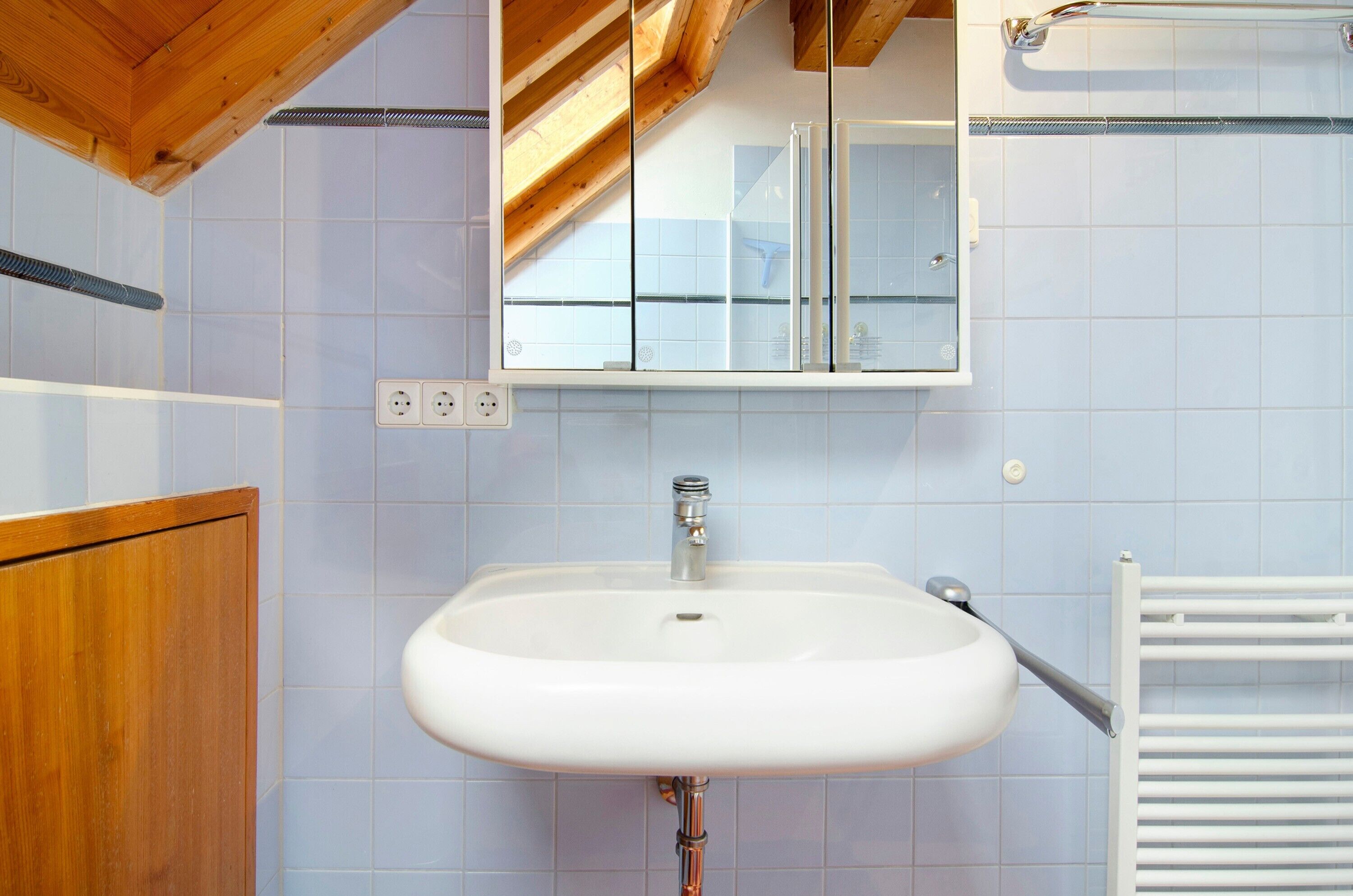 A bathroom with a white sink, wooden ceiling beams, and a white tiled wall.