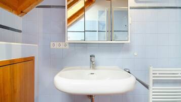 A bathroom with a white sink, wooden ceiling beams, and a white tiled wall.