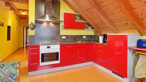 A kitchen with red cabinets, a white stove, and a wooden ceiling. - Saupp Apartment with Garden and Wi-Fi (Immenstaad am Bodensee)