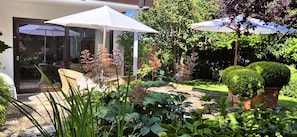 Une terrasse avec une table et des chaises, entourée de plantes en pot et d’une pelouse bien entretenue.