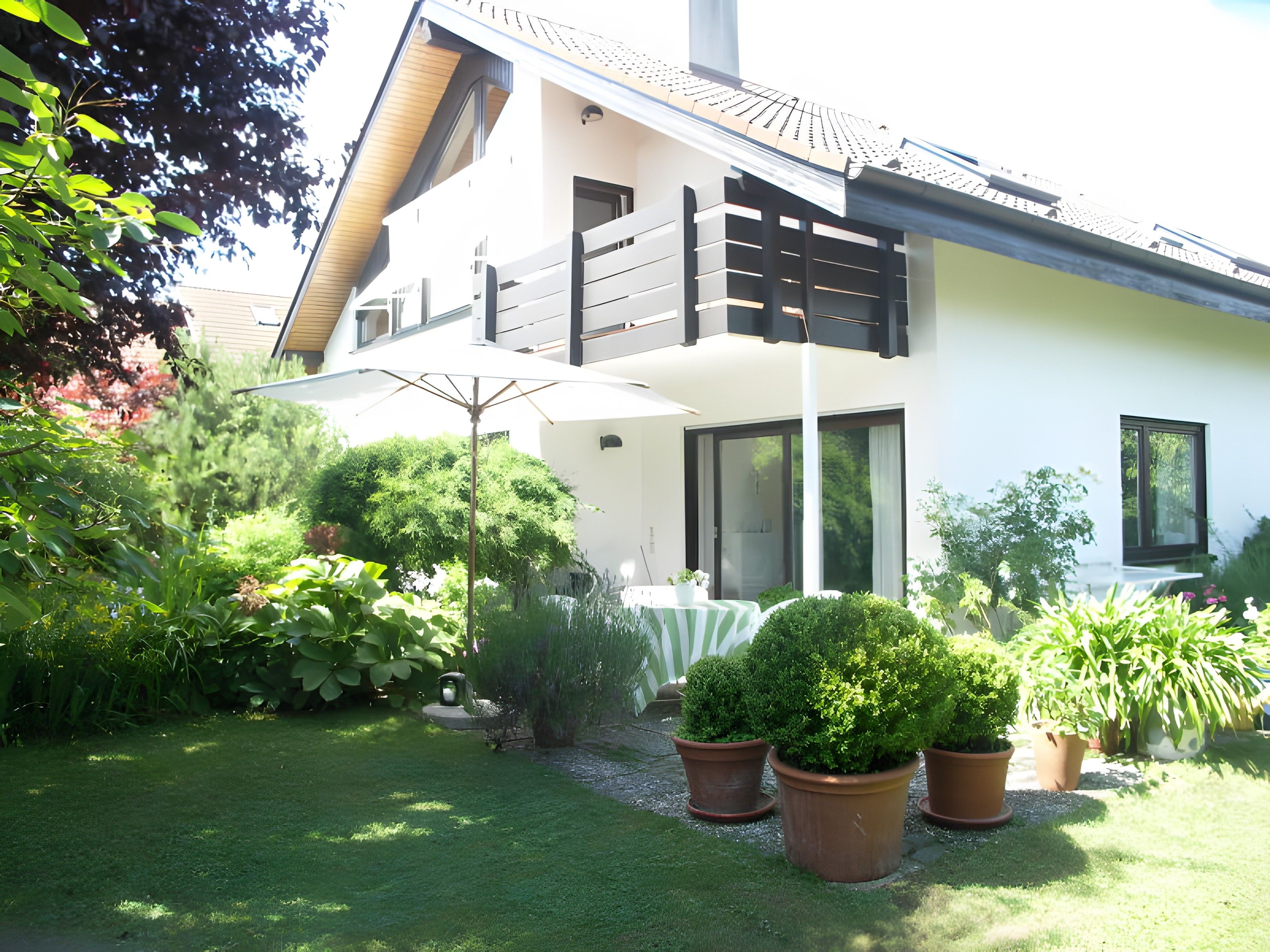 Ein modernes, zweistöckiges Haus mit Balkon, Rasen und Blumentöpfen.