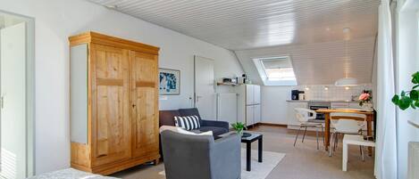 Ein modernes Wohnzimmer mit einer Couch, einem Holzschrank, einem Essbereich mit Tisch und Stühlen sowie einer Küche im Hintergrund.