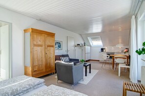A modern living room with a sofa, a wooden wardrobe, a dining area with a table and chairs, and a kitchen in the background. - Apartment Riedel '1-Room Apartment, 45 sqm' with Shared Garden, Balcony and Wi-Fi (Immenstaad am Bodensee)