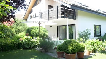 Ein modernes, zweistöckiges Haus mit Balkon, Rasen und Blumentöpfen.