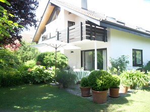 Una casa moderna de dos pisos con balcón, césped y plantas en macetas.