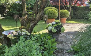 A garden with a gravel path, green plants, and neatly trimmed bushes. - Apartment Riedel '1-Room Apartment, 45 sqm' with Shared Garden, Balcony and Wi-Fi (Immenstaad am Bodensee)