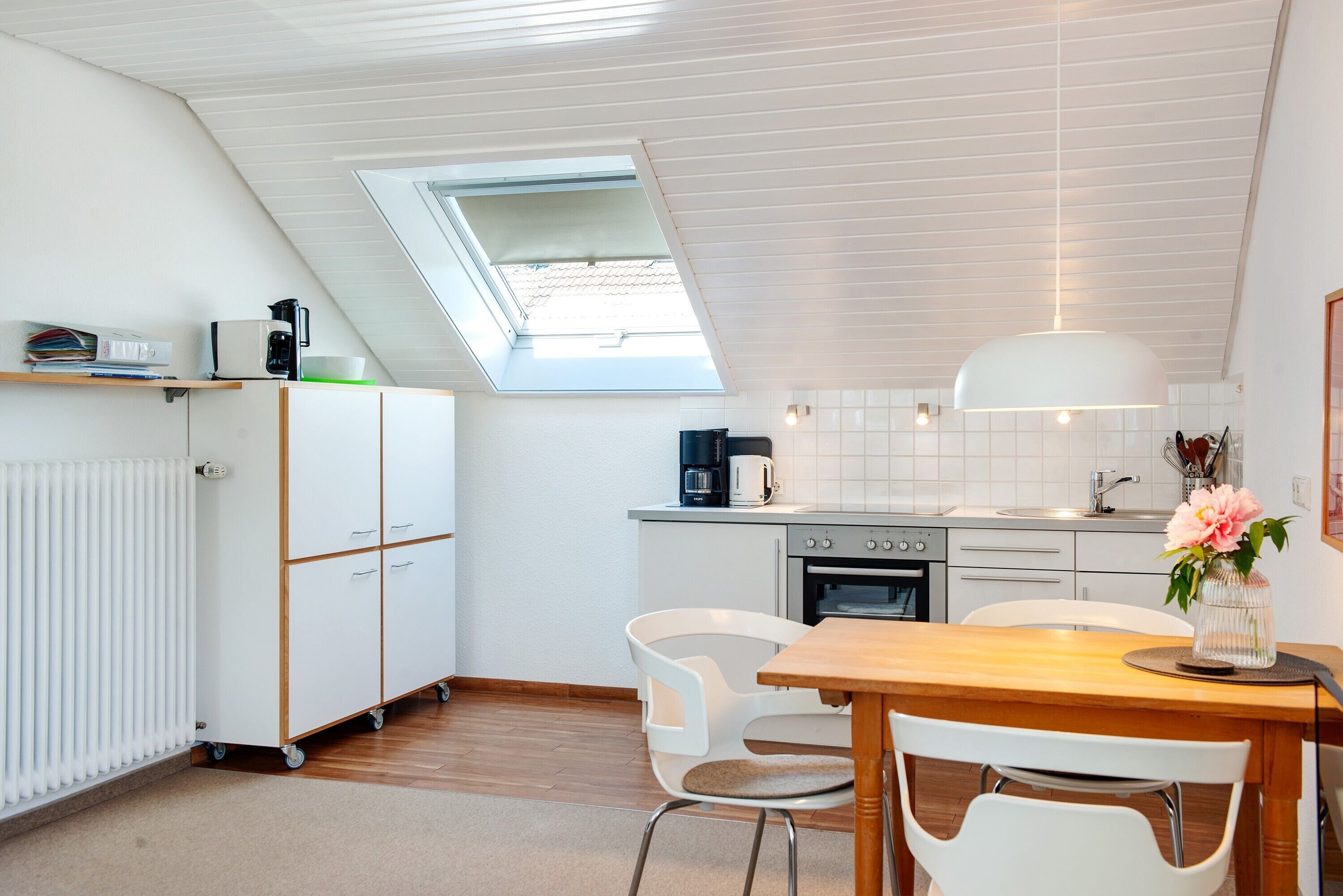 Een moderne keuken met dakraam, witte kastjes, een eettafel met stoelen en een koffieapparaat.