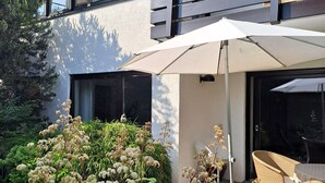 A modern two-story house with a balcony, a patio with outdoor furniture, and a garden with white flowering plants. - Apartment Riedel '1-Room Apartment, 45 sqm' with Shared Garden, Balcony and Wi-Fi (Immenstaad am Bodensee)