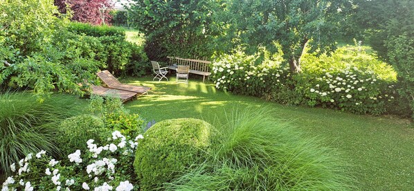 Un jardín bien cuidado con una terraza de madera, dos sillones de relax y una mesita.