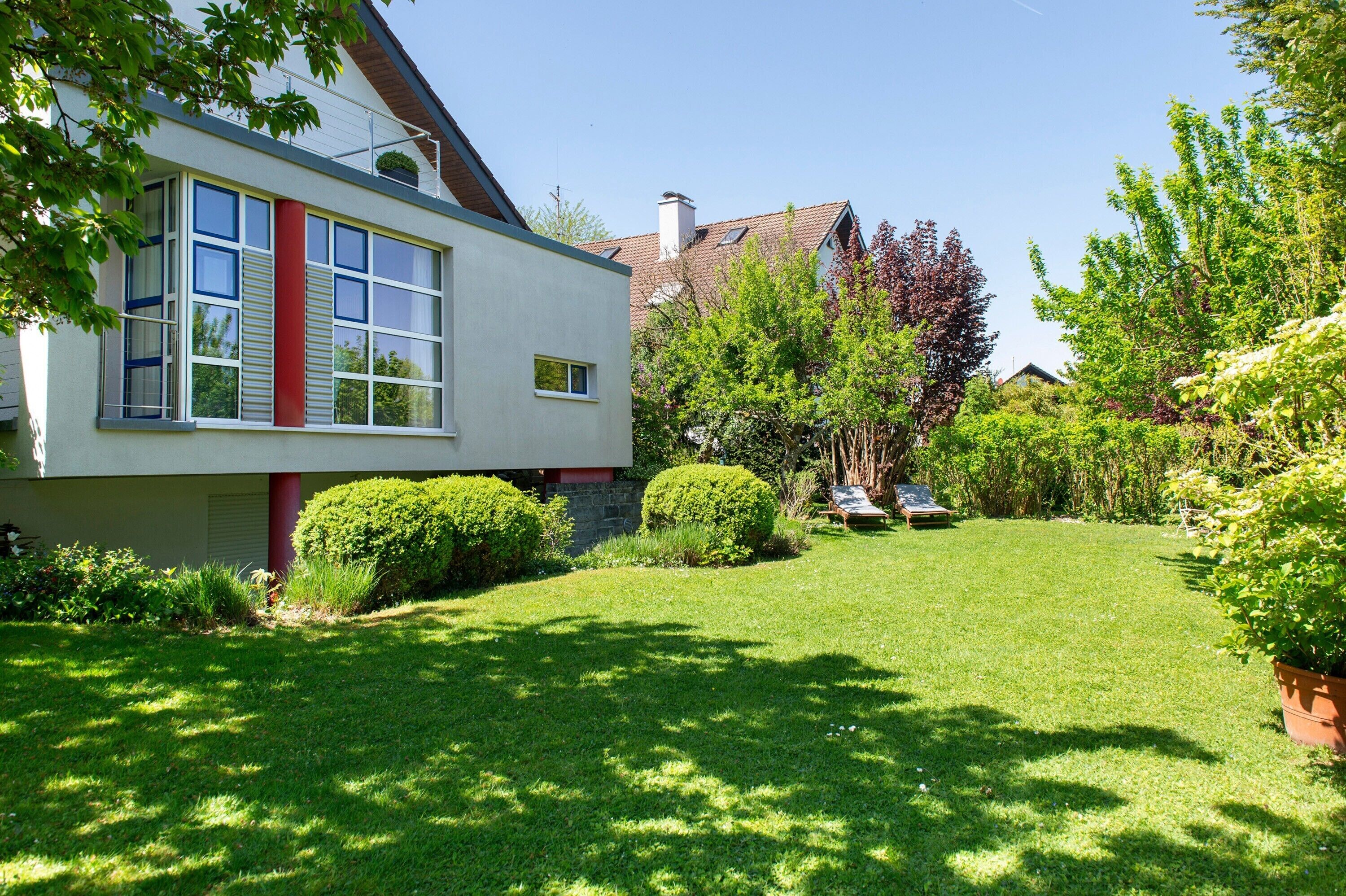 A modern house with a well-maintained lawn, a red column, and a garden with various plants.