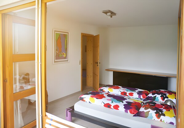 Een slaapkamer met een bed, een deur, een wandplank en een plafondlamp.