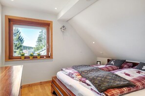 A bedroom with a large window, a bed with plaid bedding, and a wooden desk. - Holiday Apartment 'Hirschsprung Saig' with Mountain View, Wi-Fi and Air Conditioning (Lenzkirch)