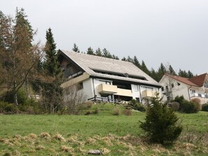 A two-story building with a sloped roof, surrounded by trees and a grassy field. - Holiday Apartment 'Hirschsprung Saig' with Mountain View, Wi-Fi and Air Conditioning (Lenzkirch)