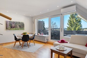 A modern living room with a dining area, large windows, and a view of trees. - Holiday Apartment 'Hirschsprung Saig' with Mountain View, Wi-Fi and Air Conditioning (Lenzkirch)