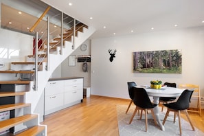 Un intérieur moderne avec un escalier, un coin repas et une décoration murale sur le thème de la forêt.