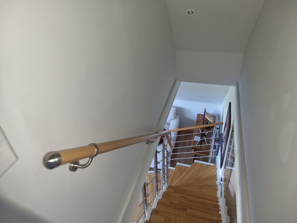 A staircase with a wooden handrail, metal railings, and a white wall.