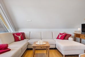 Un salon moderne avec un canapé, une petite table en bois ornée de bougies et un téléviseur posé sur un meuble en bois.