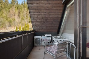 A balcony with a wooden ceiling, metal chairs, a small table, and a white air conditioning unit. - Holiday Apartment 'Hirschsprung Saig' with Mountain View, Wi-Fi and Air Conditioning (Lenzkirch)