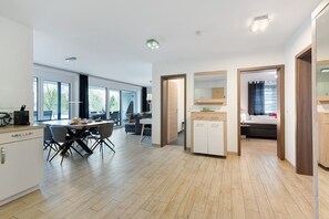 A modern kitchen with a dining area, wooden flooring, and large windows.