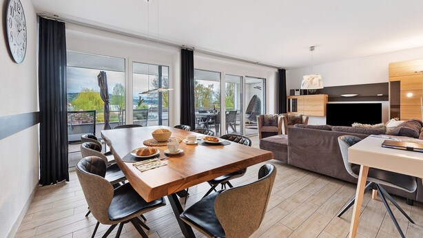 Ein modernes Wohnzimmer mit Essbereich, großen Fenstern und Blick ins Freie.