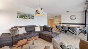 Ein modernes Wohnzimmer mit einer Eckcouch, einem Holztisch und einem Essbereich mit Stühlen und einem Tisch.