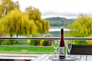 A table with a wine bottle and two glasses, overlooking a lake and trees.