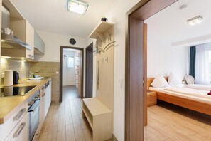 A modern kitchen with a built-in oven, a sink, and a countertop. There is a hallway leading to a bedroom with a bed and a bedside table.