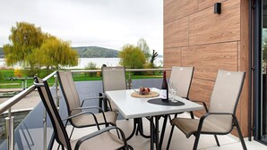 Un balcón con mesa y sillas, con vista a una masa de agua y vegetación.
