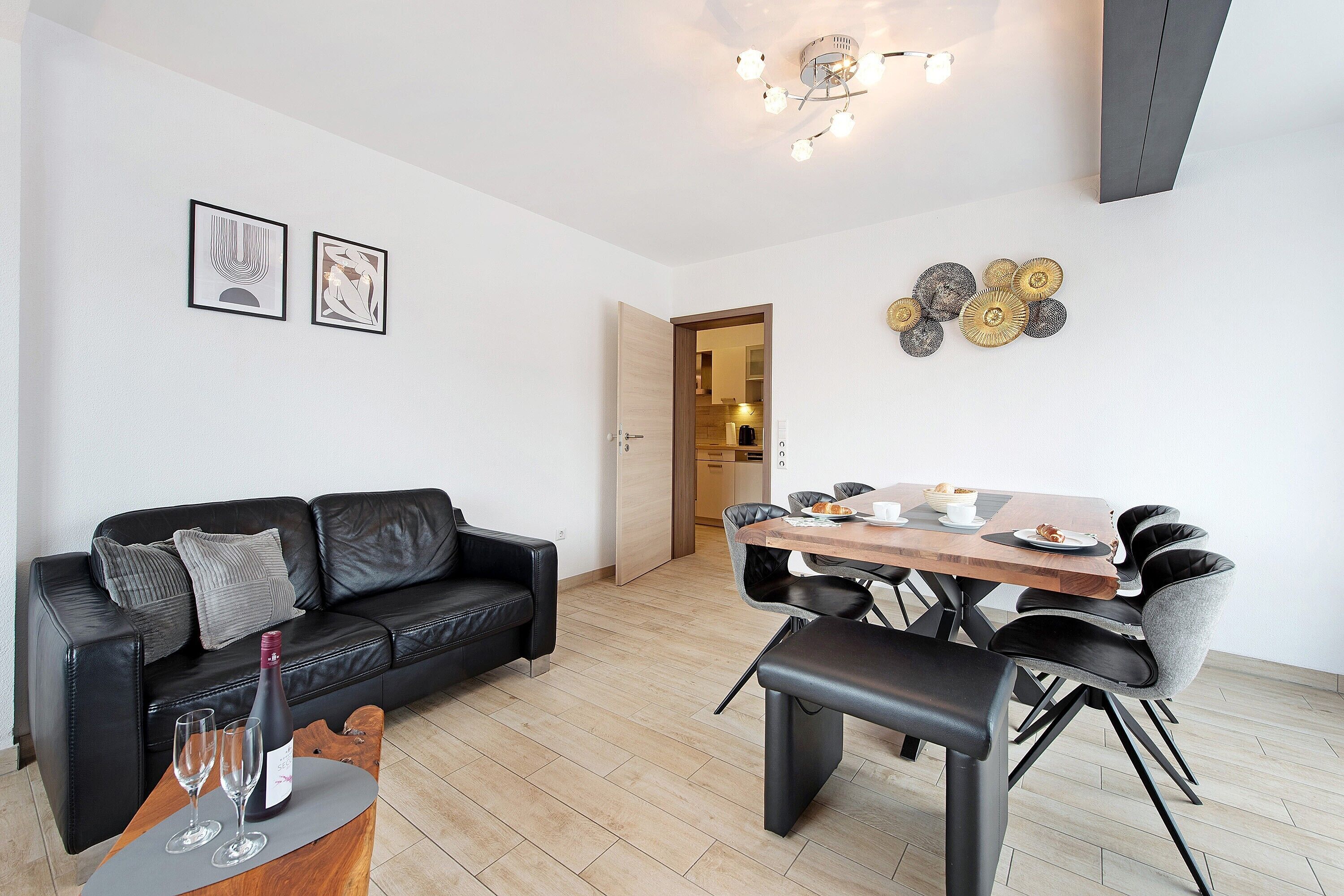 Ein modernes Wohnzimmer mit einem schwarzen Ledersofa, einem Esstisch mit Stühlen und einer Chandelier.
